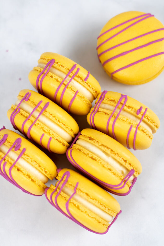 yellow macarons with red drizzle and white buttercream on marble background