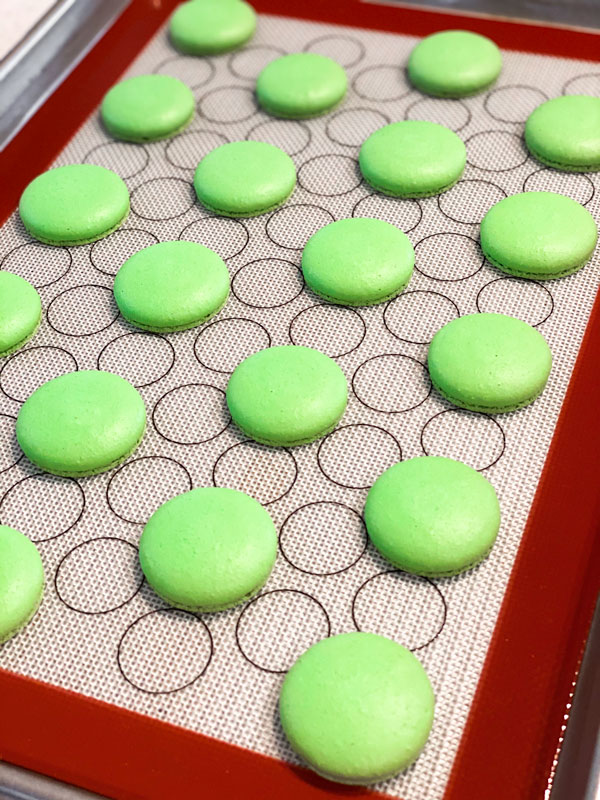 baked green macaron shells on silicone mat