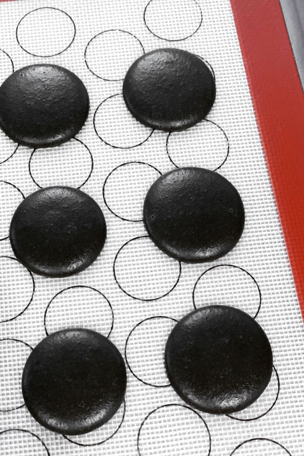 unbaked black macarons piped on silicone mat