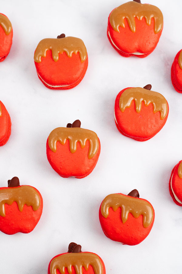 red caramel apple macarons with caramel drizzle on white background