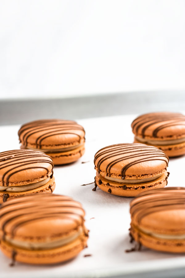 chocolate macarons with chocolate drizzle on baking sheet