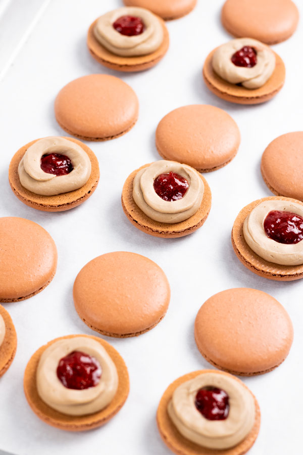 chocolate macaron shells with choclate buttercream and strawberry jam on baking sheet