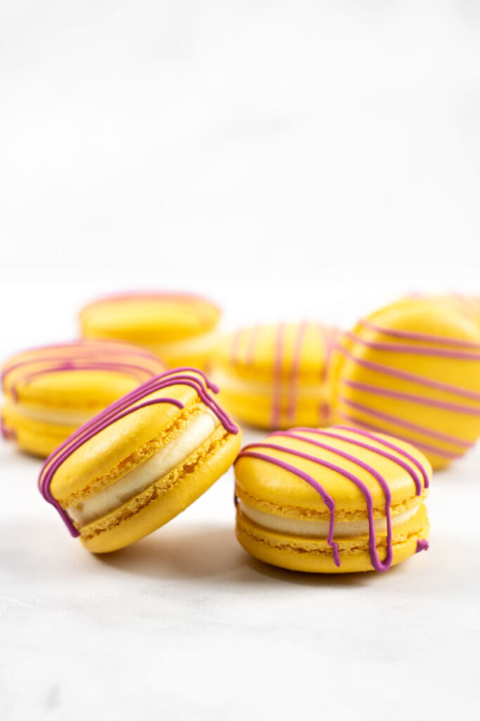 closeup of yellow macarons with red drizzle and white buttercream on white background