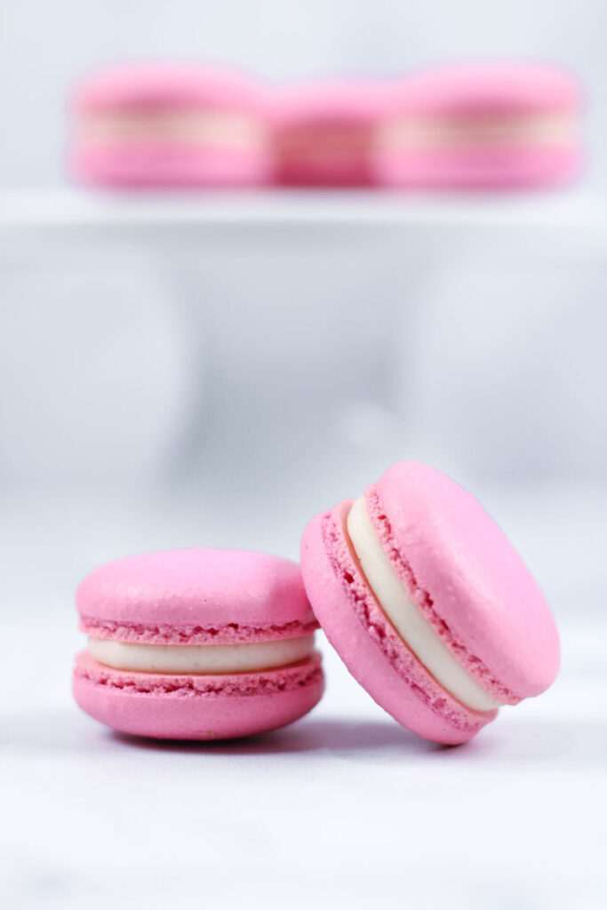 two pink vanilla macarons in front of white cakestand