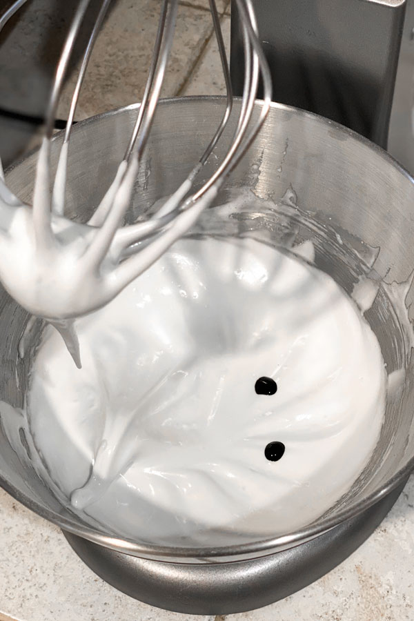 white meringue in mixing bowl with drops of food coloring