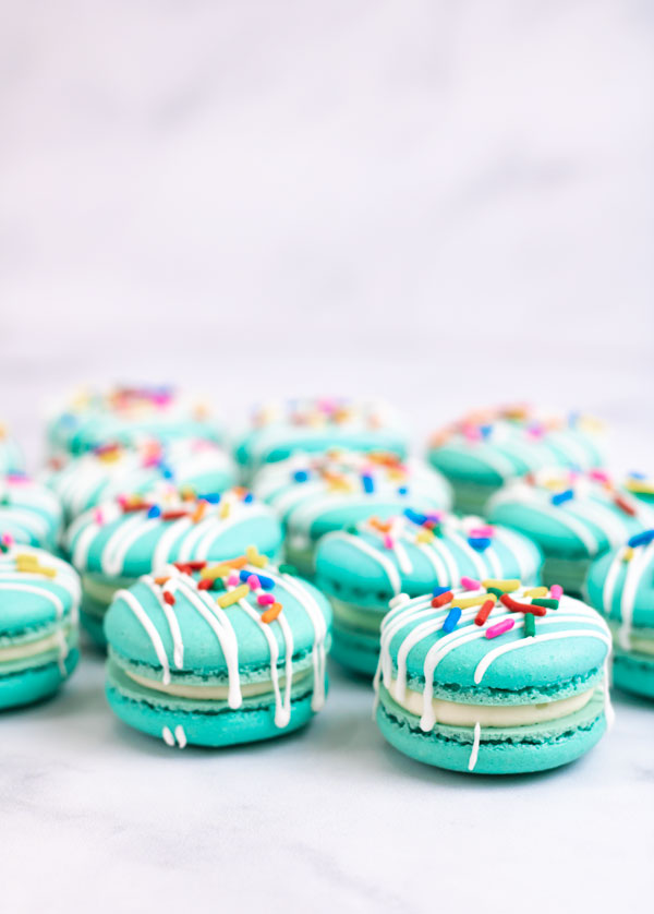 turquoise macarons with cream cheese filling with white drizzle and colorful sprinkles with white background