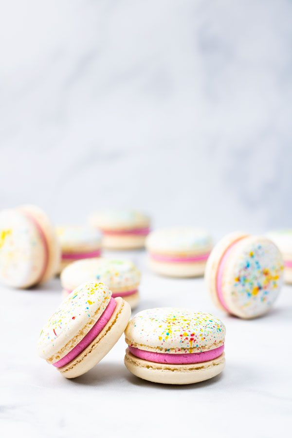 splatter paint macarons with pink buttercream in front of macarons