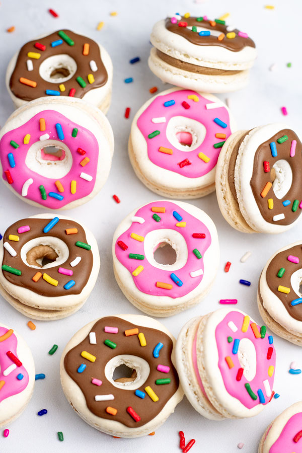 donut macarons with pink and brown decorations next to piping bags with pink and brown royal icing