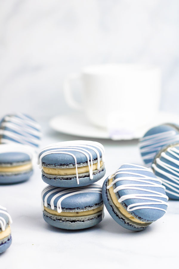 blue earl grey macarons with white drizzle in front of white teacup