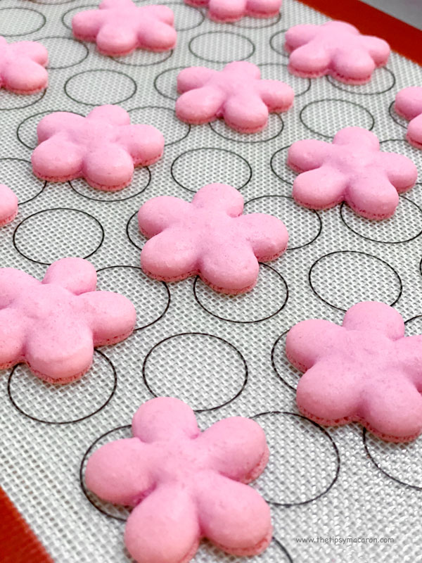 baked pink flower shaped macaron shells on silicone mat