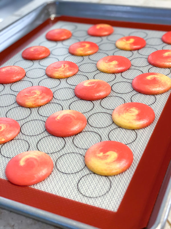 red and yellow macarons piped on silicone mat