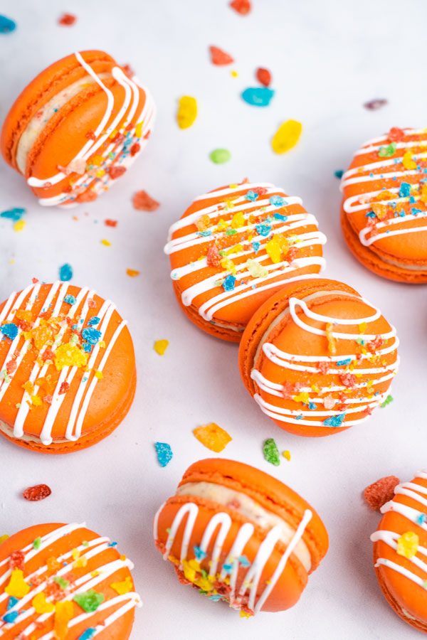 orange fruity pebbles macarons with white drizzle and cereal sprinkles on white background