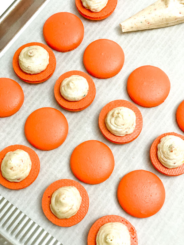 orange macaron shells with buttercream on baking tray