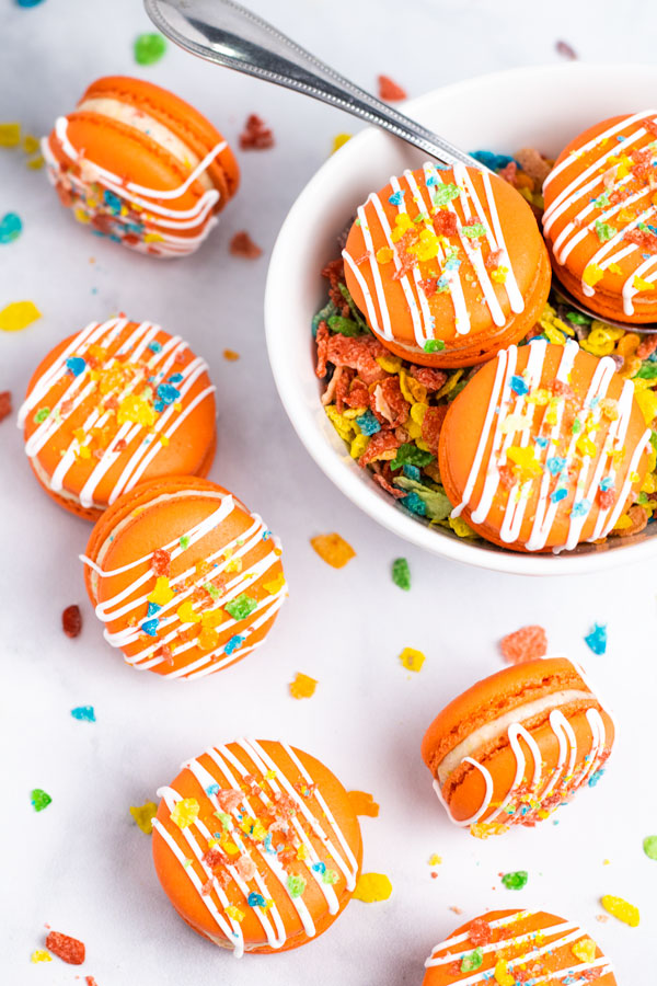 orange fruity pebbles macarons with cereal sprinkles inside cereal bowl with spoon