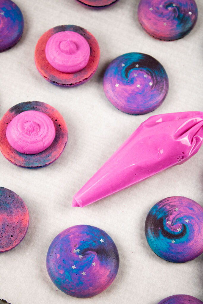 galaxy macaron shells next to pastry bag filled with pink buttercream
