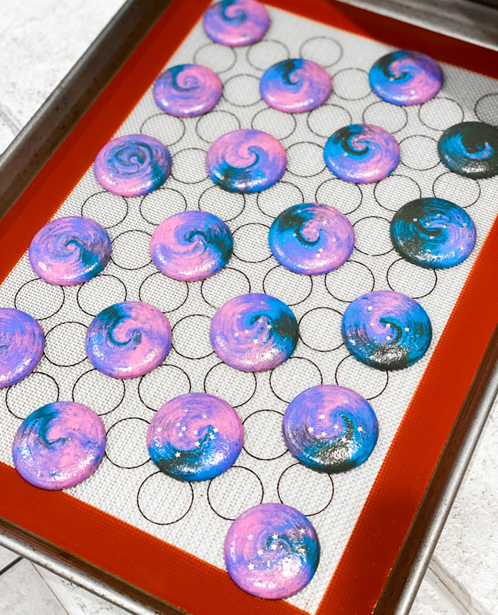 piped galaxy macaron shells on baking mat