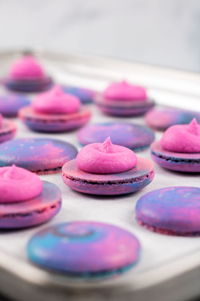 galaxy macaron shells with pink buttercream in tray