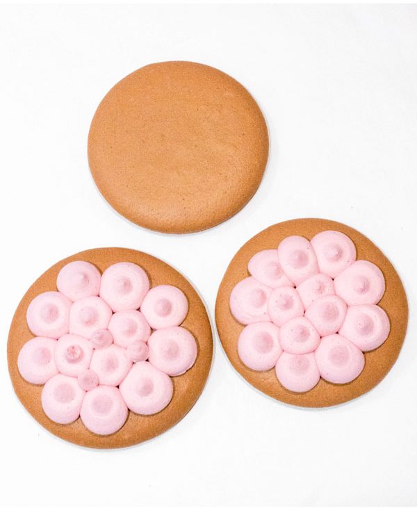 three large brown macaron shells with pink buttercream for macaron cake
