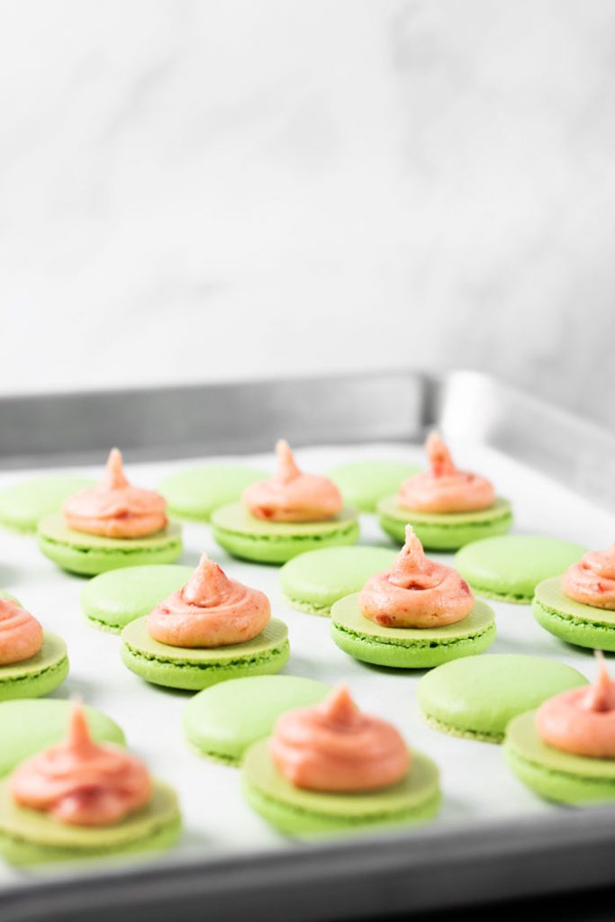 guava macaron shells with buttercream on baking tray