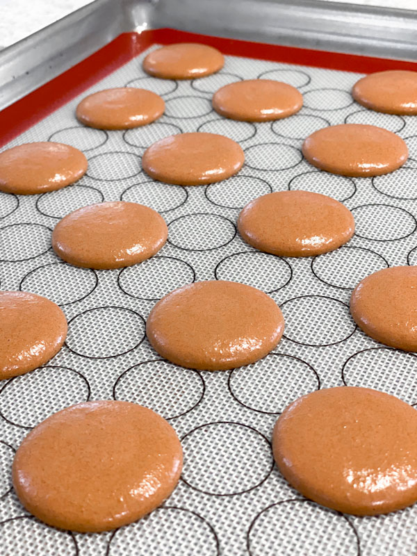 brown macaron shell batter on baking mat