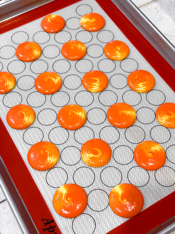 yellow and orange swirled peach macaron shells on baking sheet