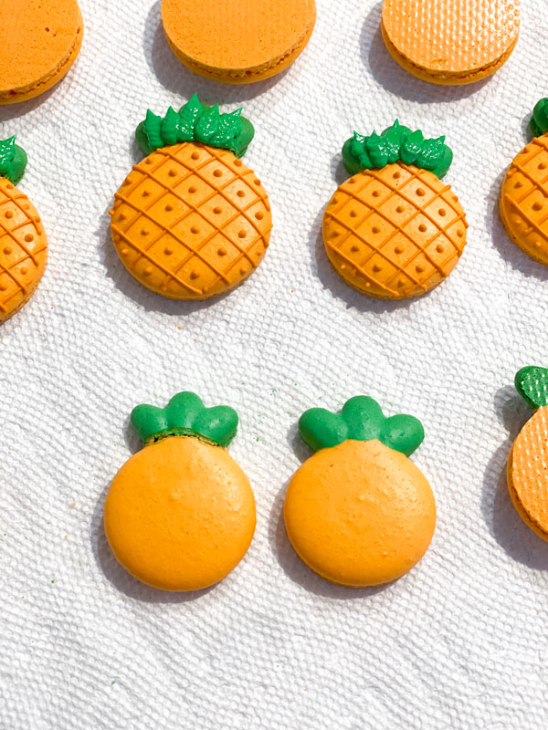 orange and green pineapple decorated macarons and two undecorated pineapple macarons