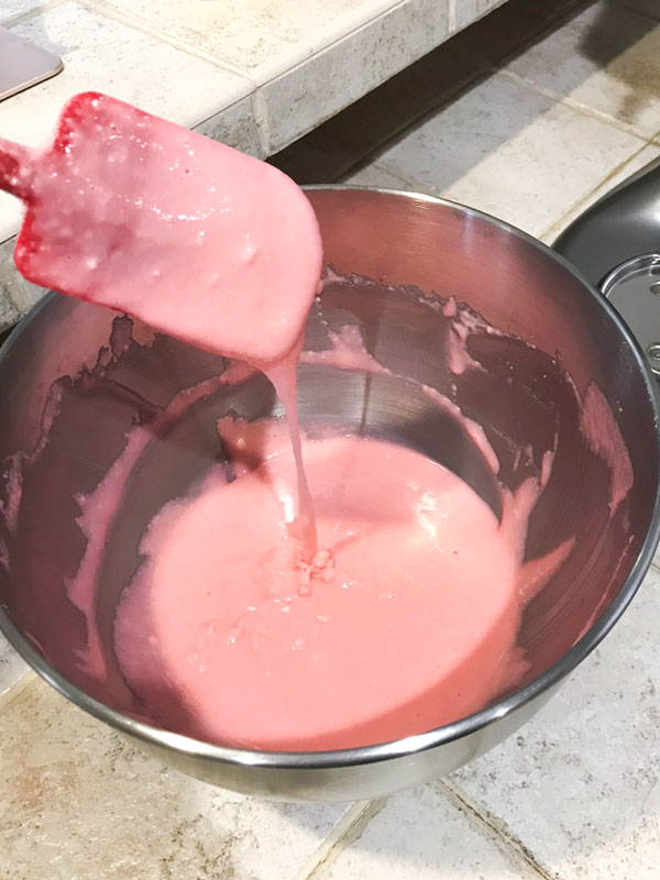 pink macaron batter in mixing bowl with red spatula