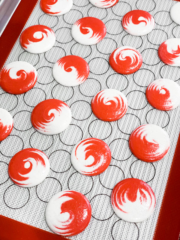 red and white macaron shells on baking mat