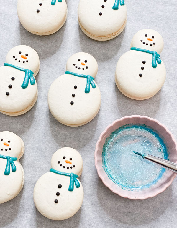 decorating snowman macaron shells with blue shimmer scarves