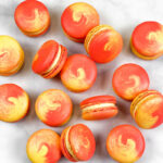 red and yellow swirled mango macarons on white and gray marble background
