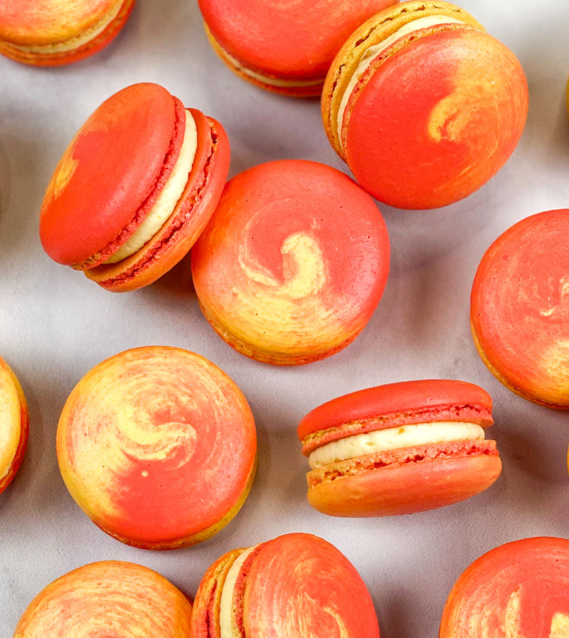 red and yellow swirled mango macarons on white and gray background