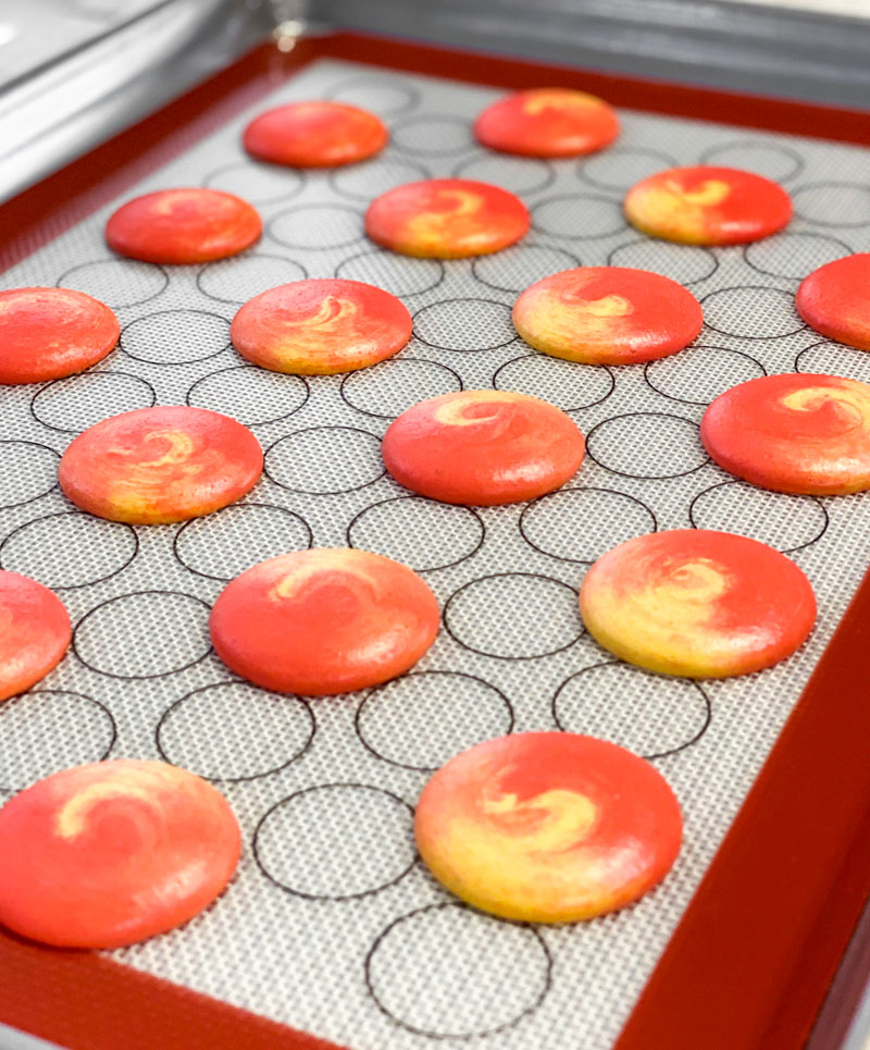 red and yellow swirled mango macarons on baking mat