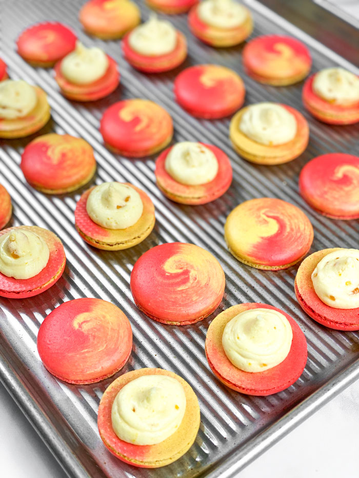 red and yellow swirled mango macarons with buttercream on baking mat