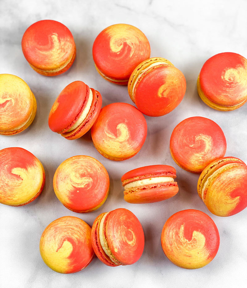 red and yellow swirled mango macarons on white and gray marble background
