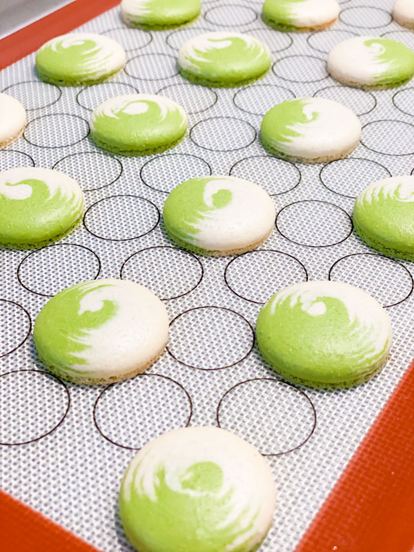 baked green and white swirled matcha macaron shells on silicone mat