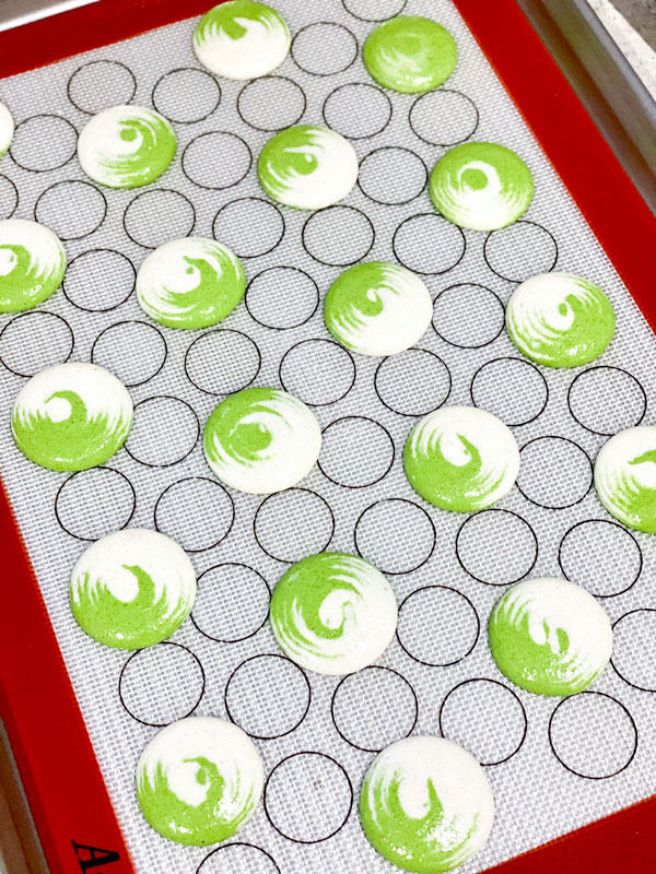 green and white swirled matcha macaron shells on silicone mat