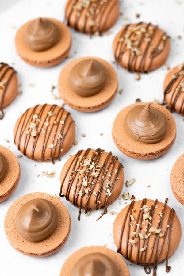 brown macaron shells filled with nutella buttercream and drizzled with chocolate and hazelnuts