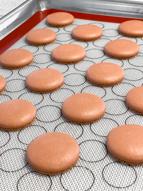 baked brown macaron shells on baking mat