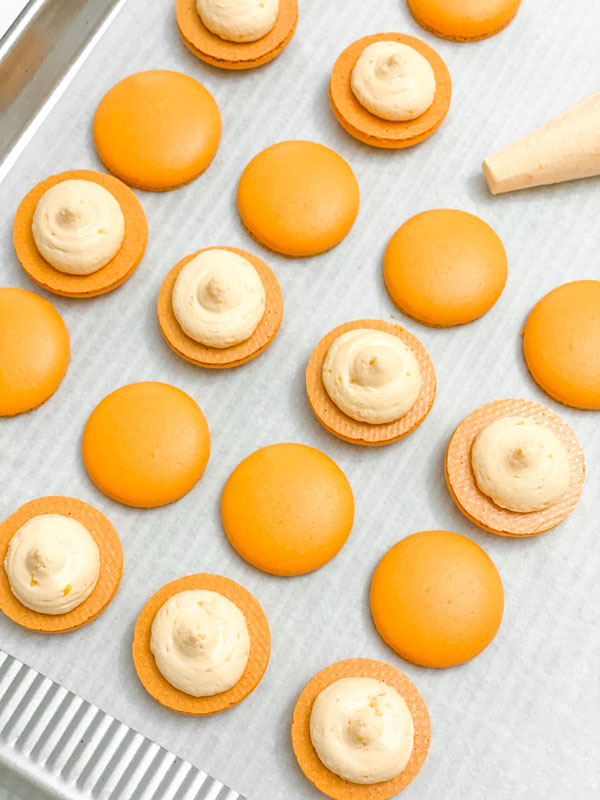 orange macaron shells with orange buttercream on parchment paper