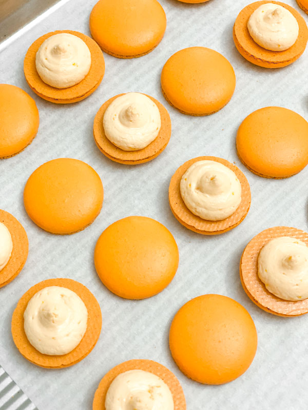 orange macaron shells with orange buttercream on baking tray