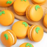 orange macarons with green leaves on wood cutting board