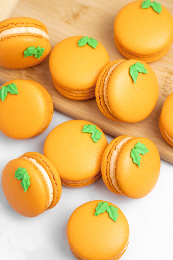 orange macarons with green leaves on wood cutting board