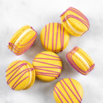 yellow macarons with red drizzle and white buttercream on marble background