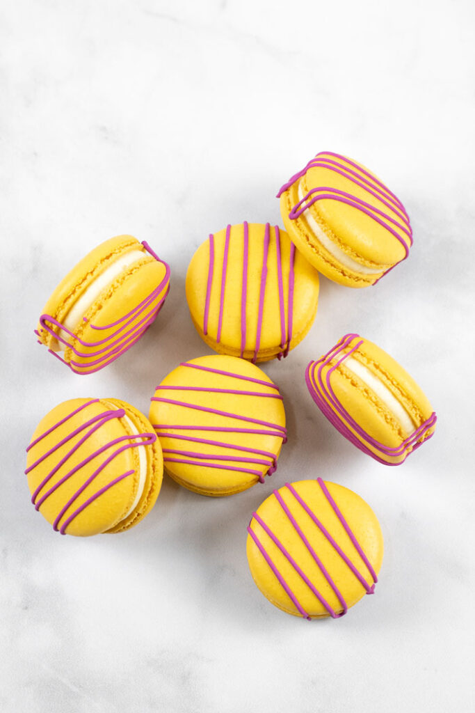 yellow macarons with red drizzle and white buttercream on marble background