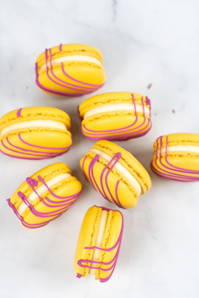 cluster of yellow macarons with red drizzle and white buttercream on marble background