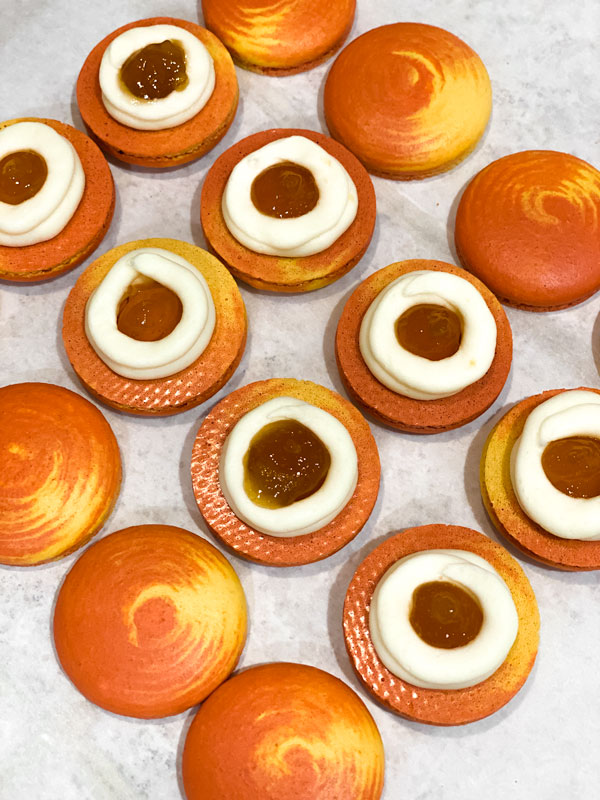 yellow and orange swirled peach macaron shells with buttercream and peach jelly