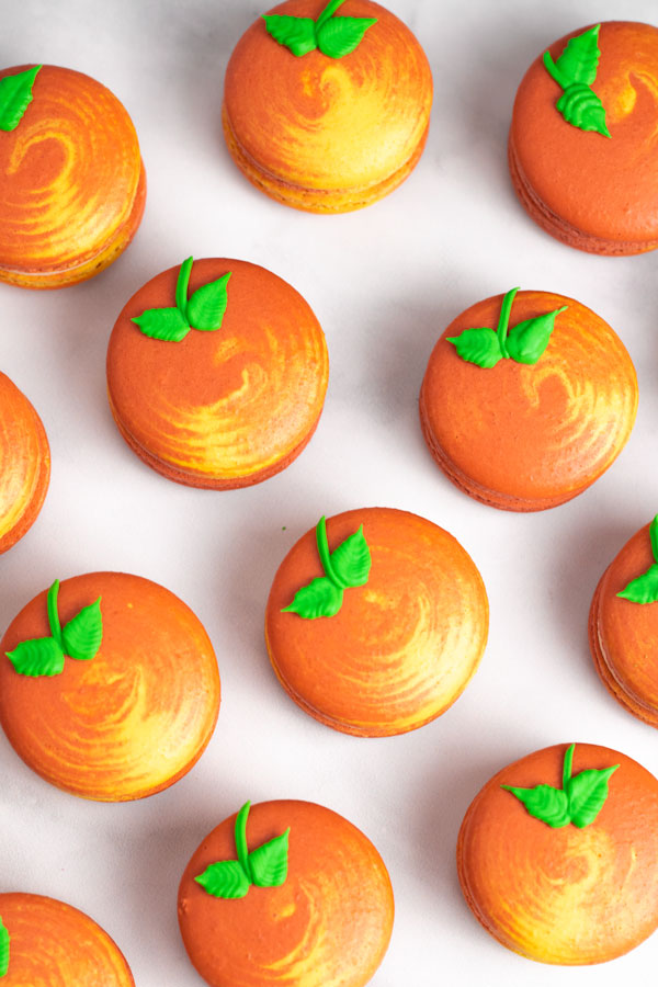 yellow and orange swirled peach macarons on white background