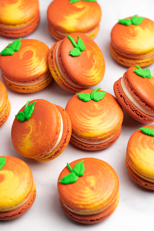 yellow and orange swirled peach macarons with green leaf icing decoration grouped together