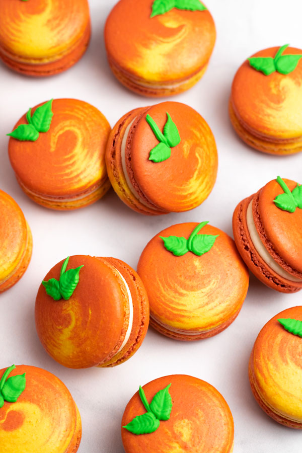 orange and yellow peach macarons with green leaf icing decoration