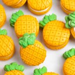 orange and green pineapple macarons scattered on white background